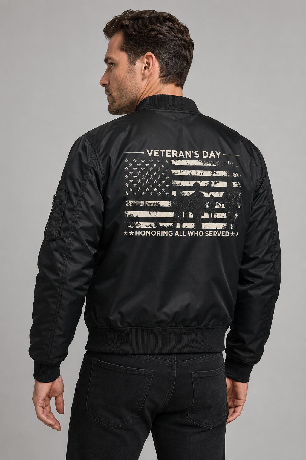 Adult model wearing Veterans Day Honoring All Who Served black bomber jacket, three-quarter back view