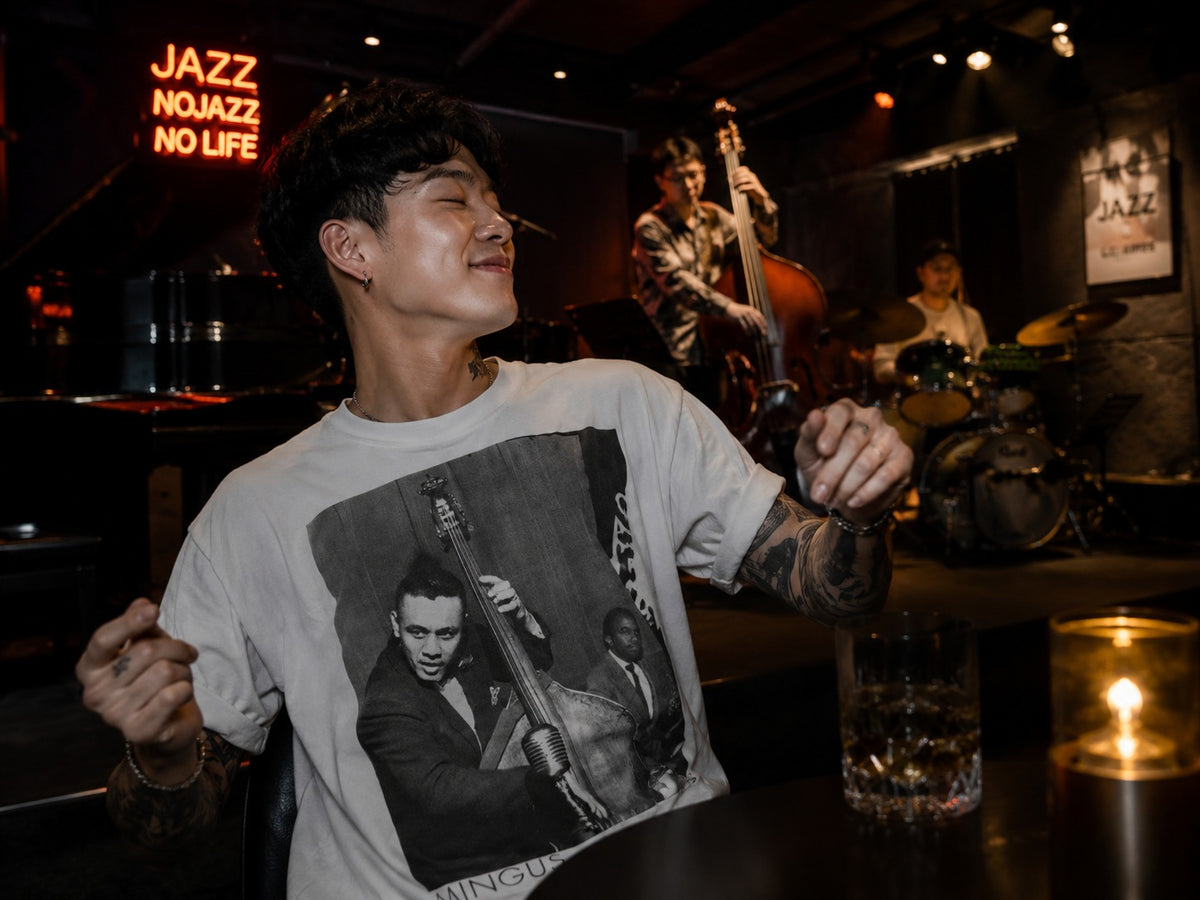 Man wearing the white Charles Mingus jazz portrait T-shirt at a live jazz club with an upright bassist and drummer